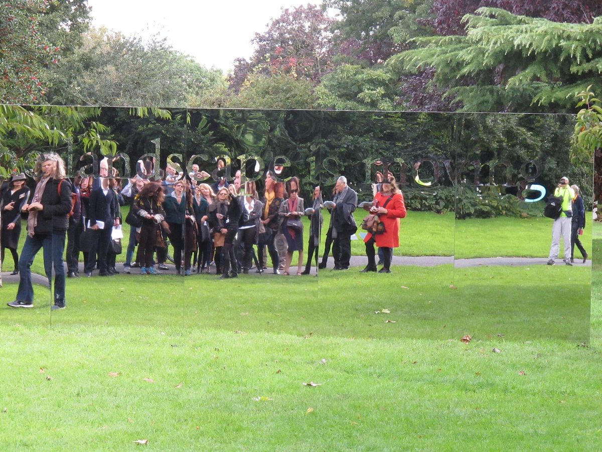A group of visitors reflected in a mirrored outdoor sculpture on the lawn of The Regent's Park